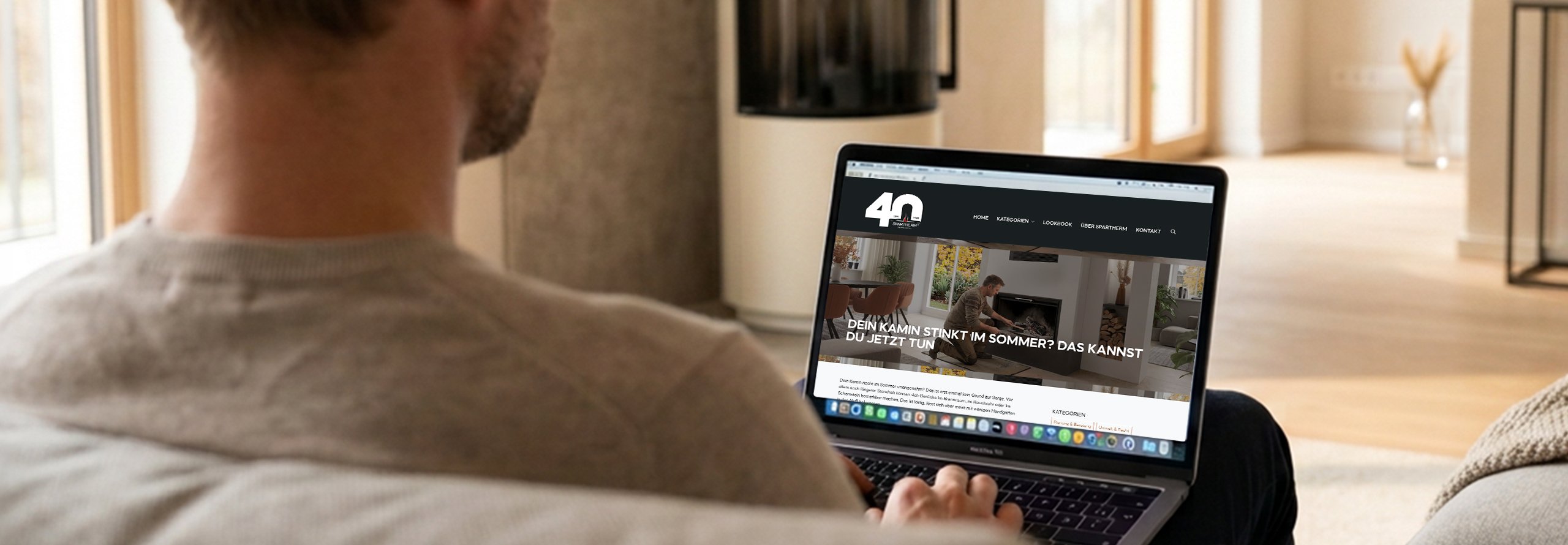 Ein Mann sitzt im Wohnzimmer auf dem Sofa und hat einen Laptop auf dem Schoß, auf dem der Blogbeitrag "Dein Kamin stinkt im Sommer?" geöffnet ist.