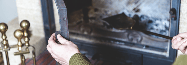 Jemand öffnet einen Kaminofen, worin sich eine Ascheschaufel befindet.
