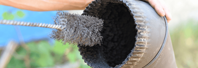 Ein Ofenrohr wird mit einer Rohrbürste gereinigt.