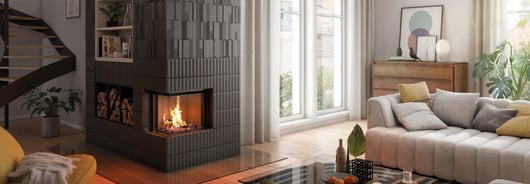 Der Kamineinsatz Premium V-2L-55h mit Holzfach steht an der Ecke eines gemütlichen Wohnzimmers.