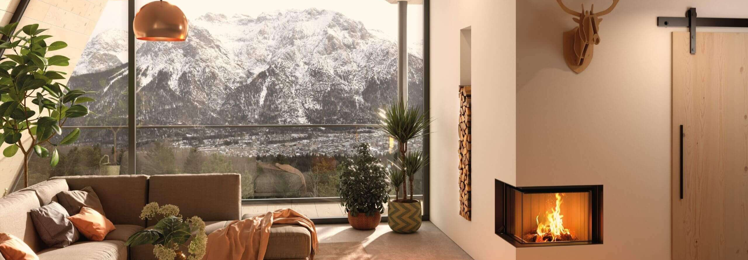 Ein weißer Kaminofen mit Holzfach steht in einem hellen Wohnzimmer neben einem großen Fenster, welches den Blick auf eine Berglandschaft freigibt.