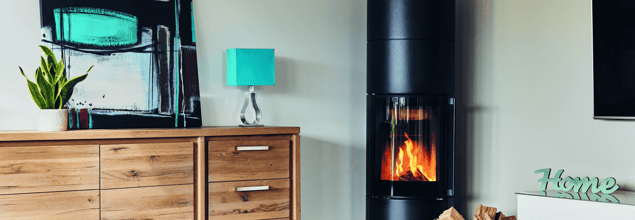 Ein wasserführender Kaminofen steht in der Ecke eines modernen Wohnzimmer neben einer Kommode.