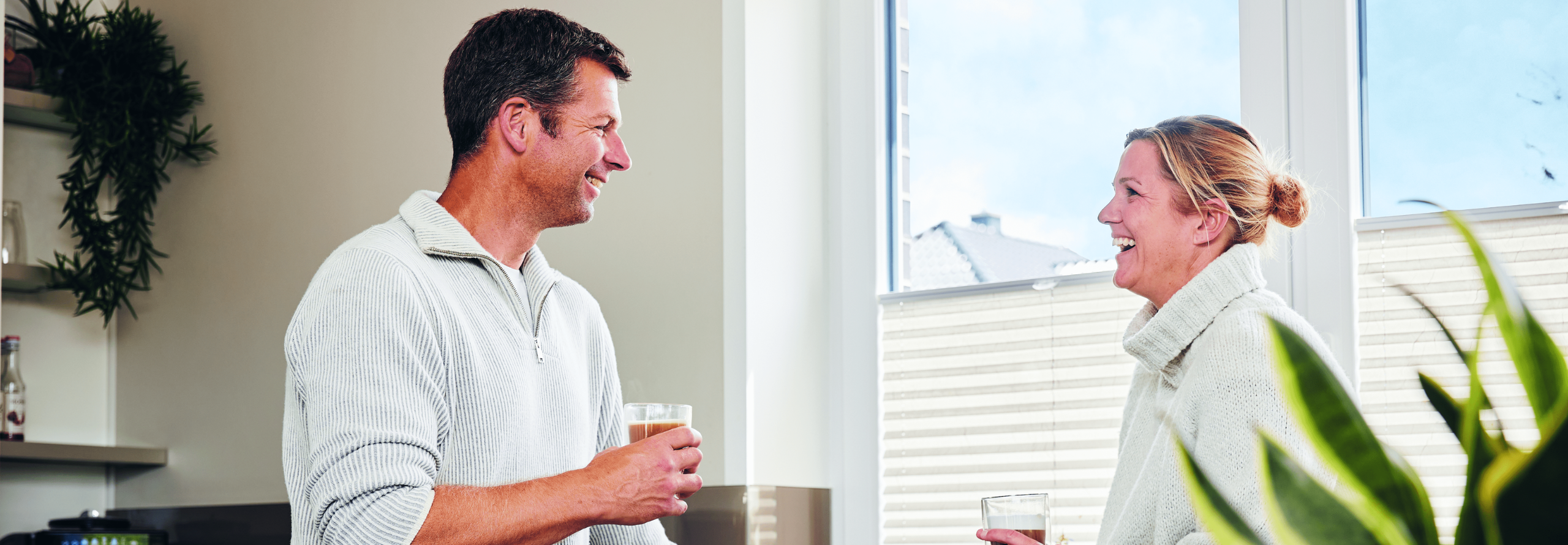 Herr und Frau Jachens unterhalten sich, halten beide ein Getränk in der Hand und lachen dabei.