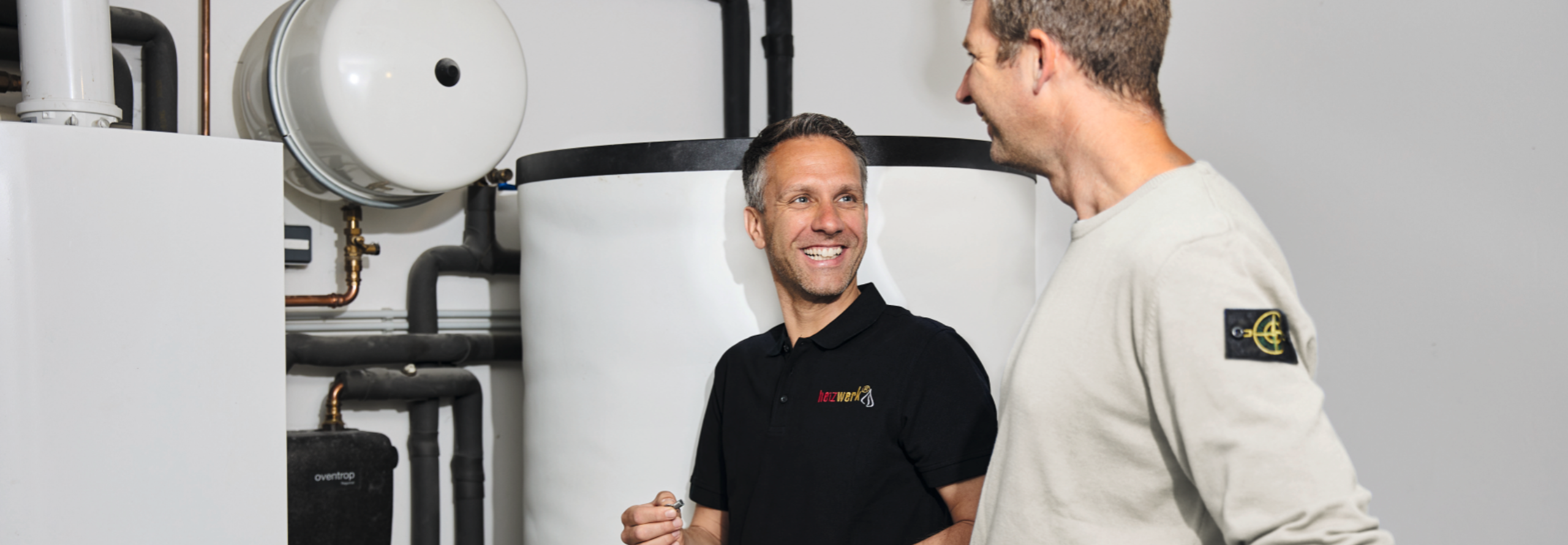 Herr Jachens unterhält sich mit einem Fachmann für Heizungstechnik in einem Heizungskeller.