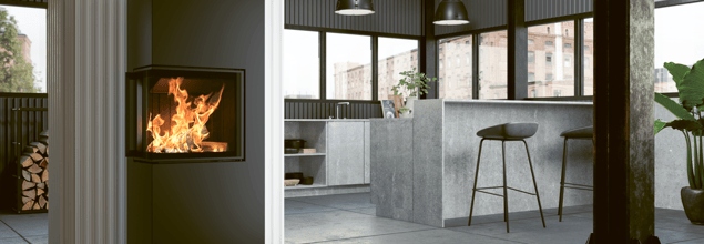 Der Lungo 2L/2R Kaminofen steht vor einer weißen Wand, die als Raumteiler zur Küche dient.