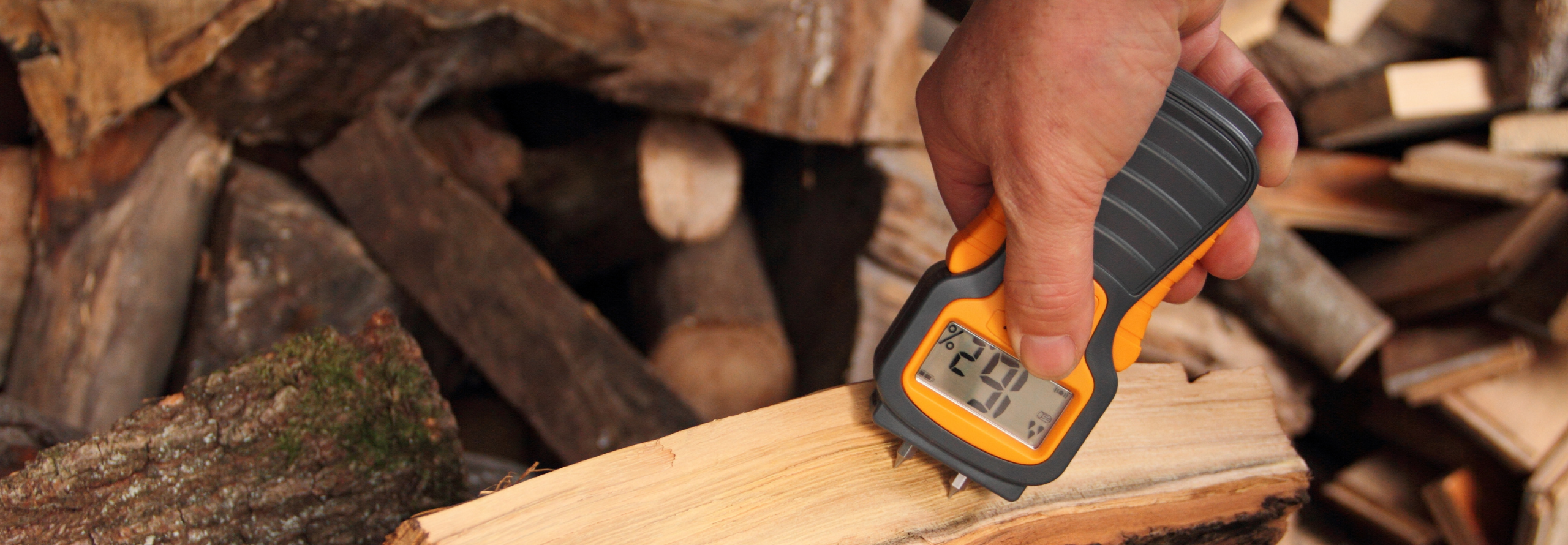 Mit einem Holzfeuchtemessgerät wird die Feuchte eines Holzscheites gemessen.